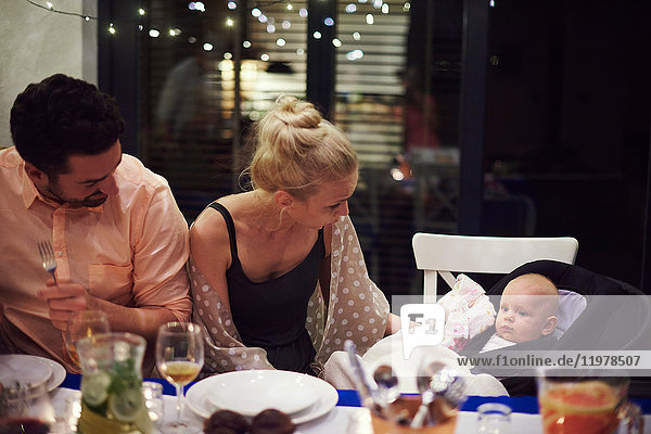 Couple sitting at dinner table  tending to baby daughter