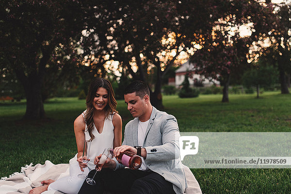 Romantisches junges Paar schenkt in der Abenddämmerung rosa Champagner im Park ein