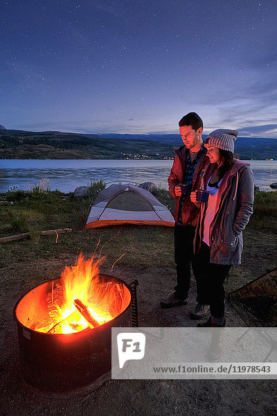 Couple standing near campfire. at dusk  drinking hot drinks