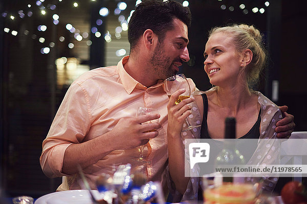Couple sitting at table  holding wine glasses  face to face  smiling