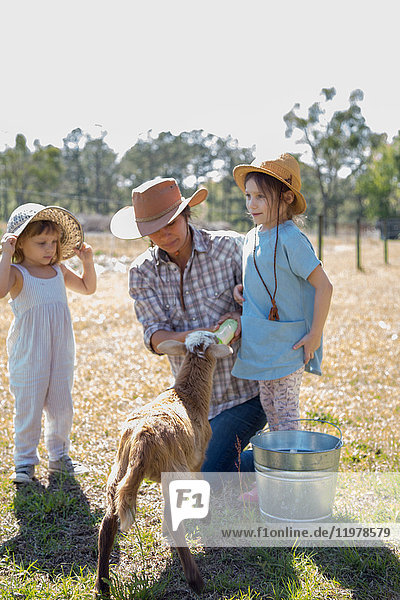 Mutter und zwei Kinder auf dem Bauernhof,  Flaschenfütterung junger Ziegen