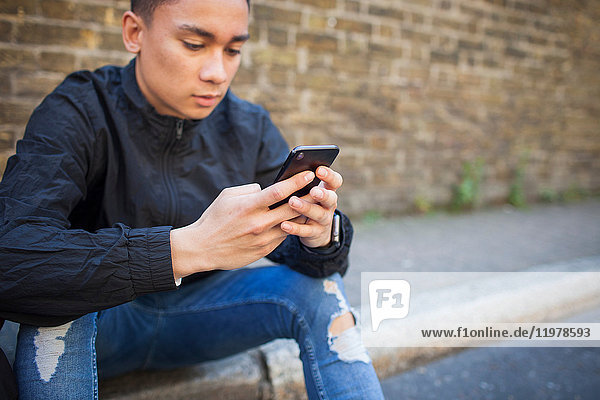 Junger Mann sitzt im Freien und benutzt ein Smartphone