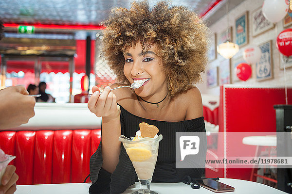 Portrait of young woman sitting in diner  eating icecream dessert  smiling