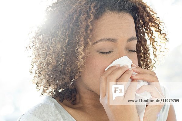 Mid adult woman blowing nose on tissue.