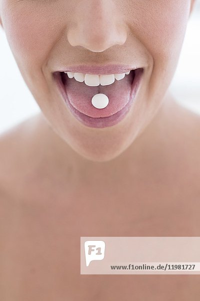 MODELL FREIGEGEBEN. Junge Frau mit Pille auf der Zunge.