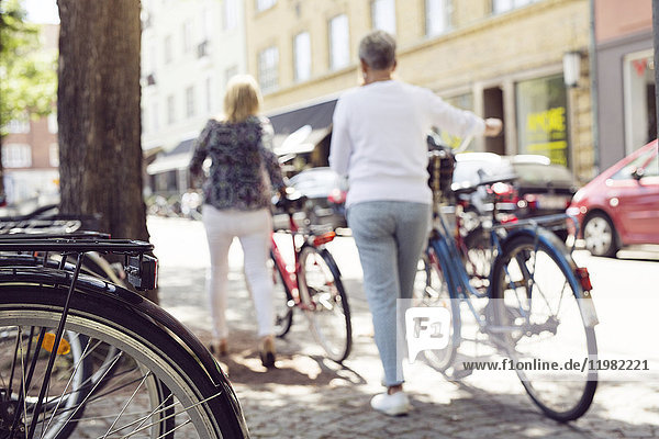 Two women pushing bikes in city
