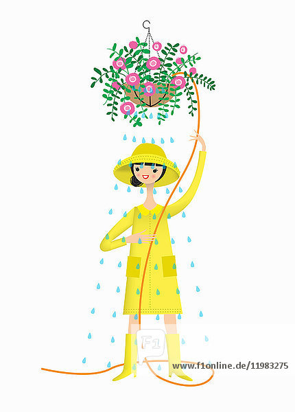 Frau mit Regenhut,  Regenmantel und Gummistiefeln,  um einen Hängekorb zu gießen