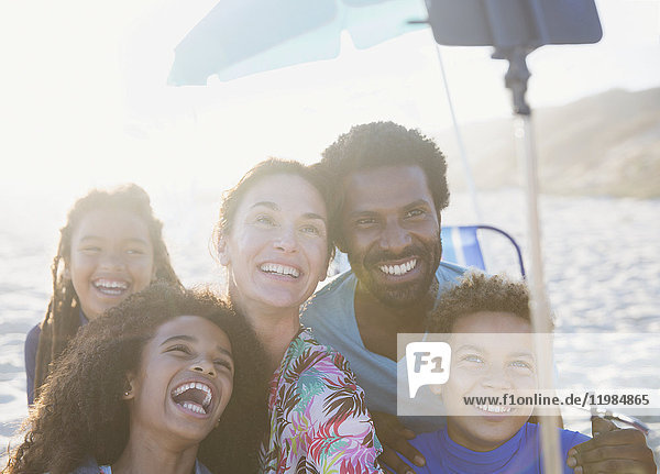 Fröhliche,  verspielte multiethnische Familie mit Selfie-Stick am sonnigen Sommerstrand
