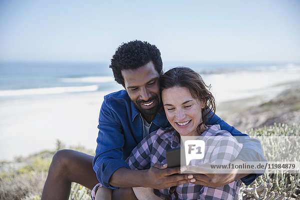 Smiling multi-ethnic couple taking selfie with cell phone on summer beach