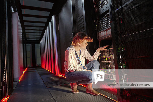 Female IT technician examining panel in dark server room