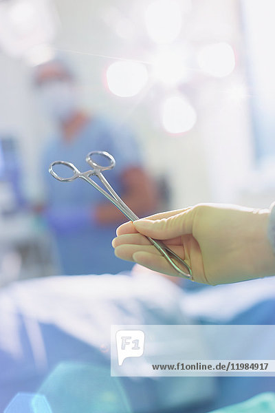 Chirurg mit Gummihandschuh  der eine chirurgische Schere im Operationssaal hält