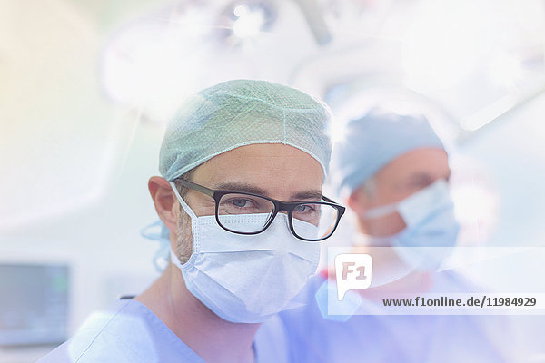 Porträt eines selbstbewussten männlichen Chirurgen mit Brille und chirurgischer Maske im Operationssaal