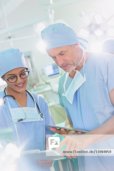 Chirurgen mit digitalem Tablet und Klemmbrett im Gespräch im Operationssaal