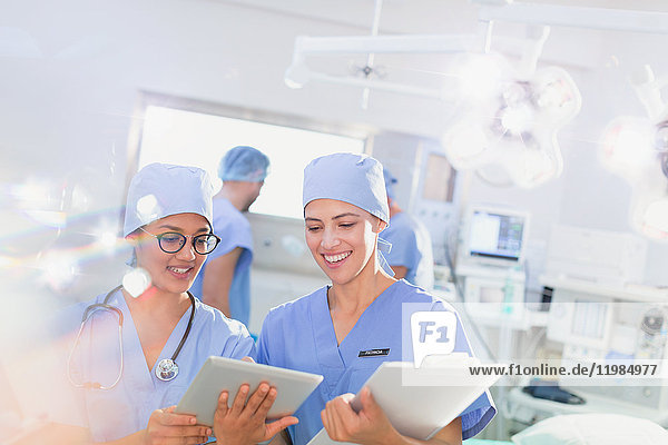 Smiling female surgeons using digital tablet and clipboard in operating room