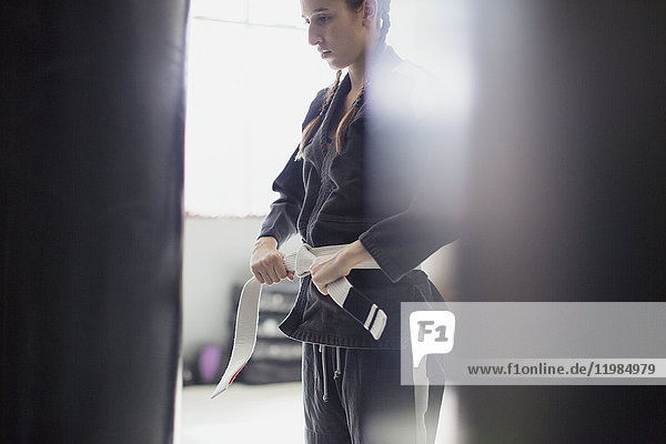 Junge Frau beim Binden des Judogürtels im Fitnessstudio