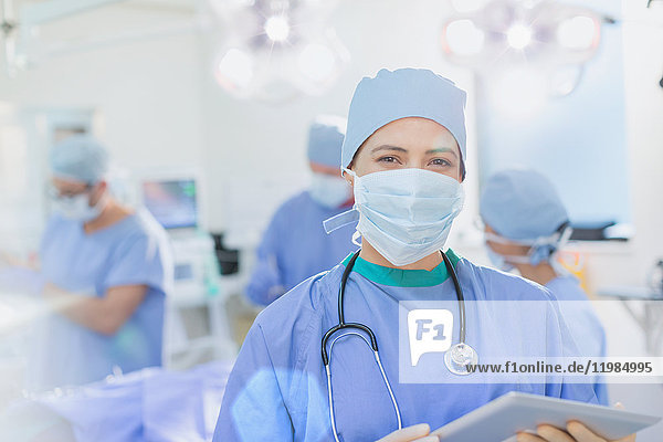 Porträt einer selbstbewussten Chirurgin mit chirurgischer Maske und digitalem Tablet im Operationssaal