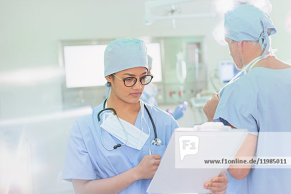 Chirurgin  die im Operationssaal Papierkram auf einem Klemmbrett überprüft
