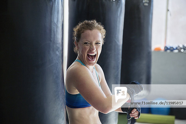 Portrait exuberant female boxer screaming  wrapping wrists in gym
