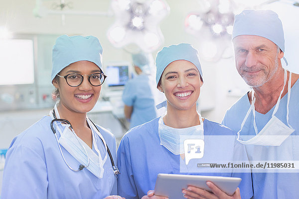 Porträt lächelnder  selbstbewusster Chirurgen mit digitalem Tablet im Operationssaal
