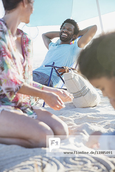 Smiling man relaxing with hands behind head on summer beach with family