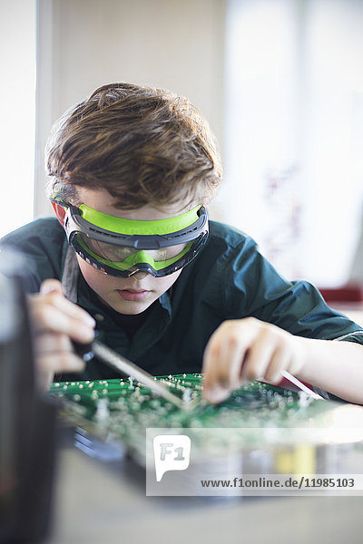 Fokussierter Schüler in Brille lötet Leiterplatte im Klassenzimmer