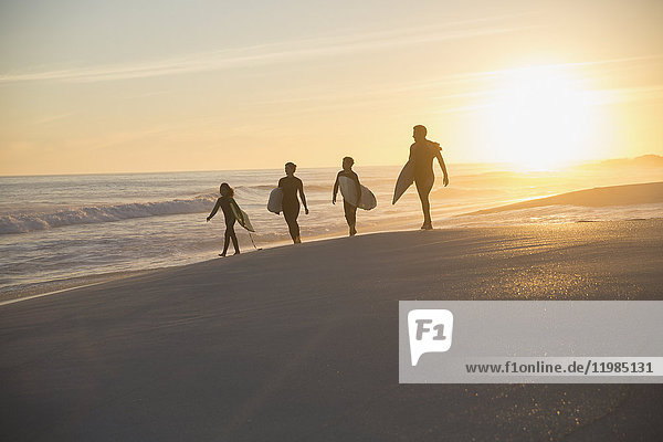Silhouette family surfers walking with surfboards on sunny summer sunset beach