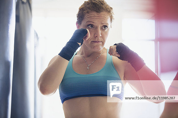 Entschlossene Boxerin mit Handgelenksbandagen in Kampfstellung im Fitnessstudio