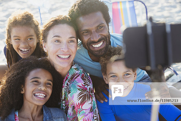 Lächelnde  fröhliche multiethnische Familie  die Selfie mit Selfie-Stick-Kamera-Handy am Strand nimmt.