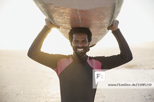 Portrait smiling  confident male surfer carrying surfboard overhead on sunny summer beach