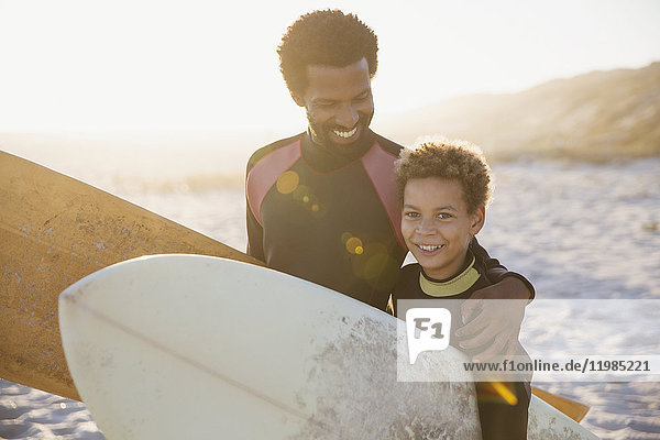 Portrait smiling father and son surfers carrying surfboards on sunny summer beach