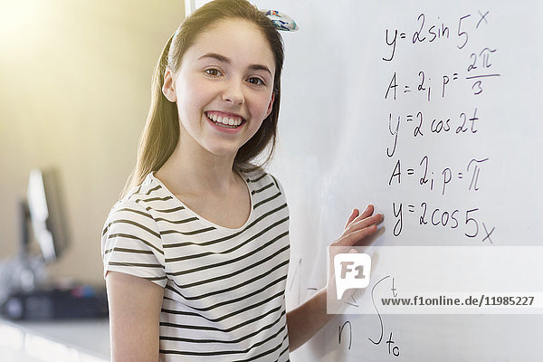 Portrait lächelndes  selbstbewusstes Mädchen  das die Physik-Gleichung am Whiteboard im Klassenzimmer löst.