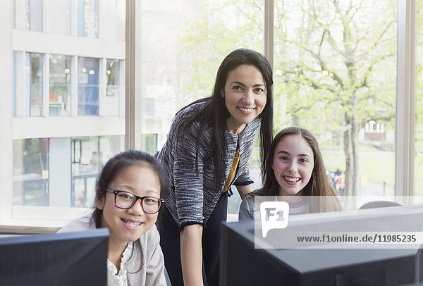 Portrait selbstbewusste  lächelnde Lehrerin und Schülerinnen beim Recherchieren am Computer in der Bibliothek