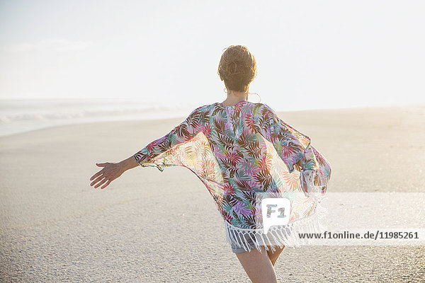 Carefree woman walking with arms outstretched on summer beach
