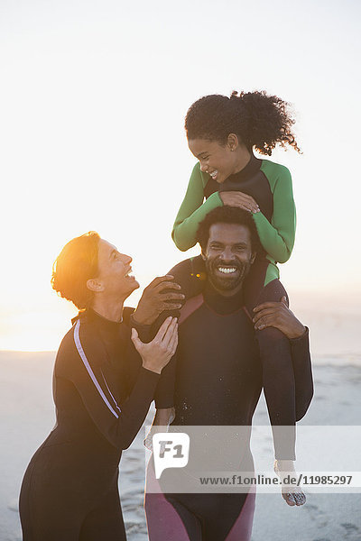Happy family in wet suits on summer sunset beach