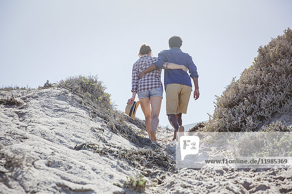 Affectionate couple walking up sandy sunny summer beach path