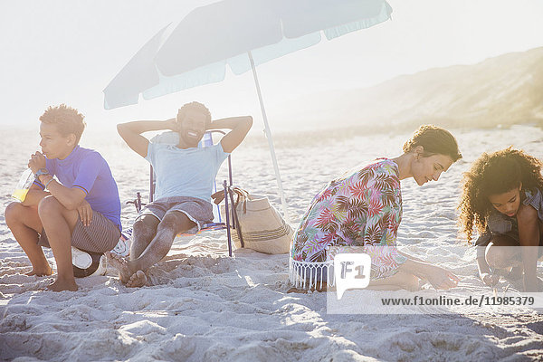 Multi-ethnische Familie entspannt sich und spielt im Sand am sonnigen Sommerstrand.