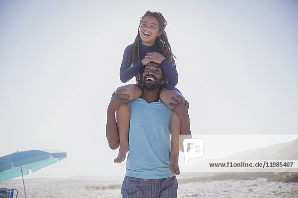 Playful father carrying daughter on shoulders on sunny summer beach