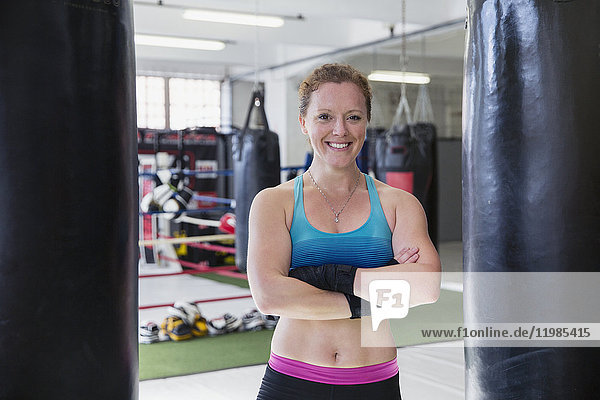 Portrait smiling  confident female boxer standing at punching bags in gym