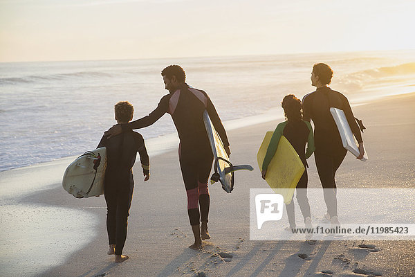 Familien-Surfer wandern mit Surfbrettern am sonnigen Sommer-Sonnenuntergangsstrand