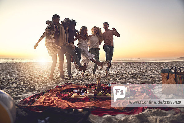 Verspielte junge Freunde beim Kicken  Picknick am sonnigen Sommer-Sonnenuntergangsstrand