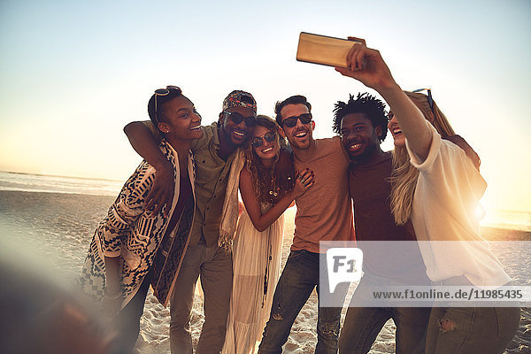 Young friends with camera phone taking selfie on sunny summer beach