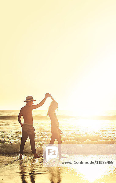 Junges Paar hält sich an den Händen und geht am sonnigen Sommer-Sonnenuntergangstrand spazieren.
