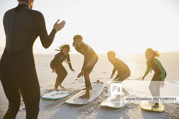 Surfer instructor teaching family on surfboards surfing on sunny summer sunset beach