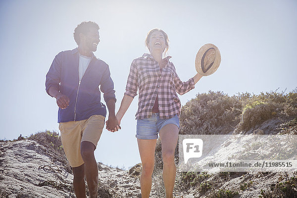Multi-ethnic couple walking  holding hands on sunny summer beach path