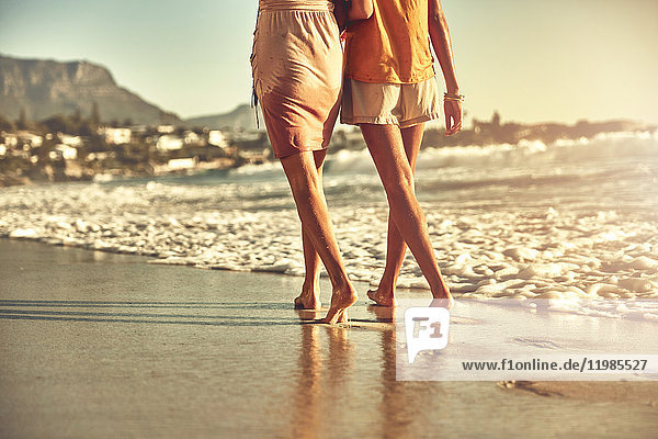 Barefoot young women walking on sunny summer ocean beach