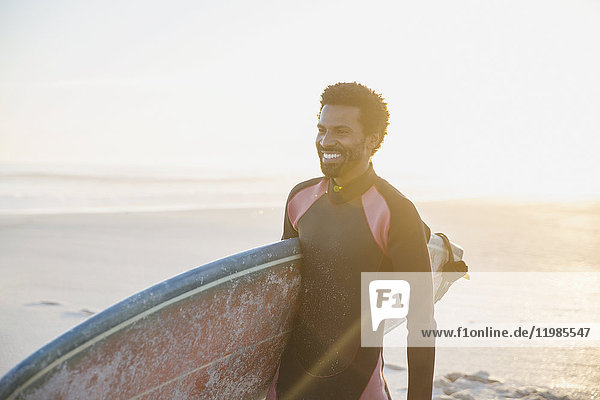 Lächelnder Surfer mit Surfbrett am sonnigen Sommerstrand
