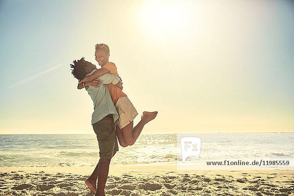 Playful boyfriend lifting girlfriend on sunny summer ocean beach