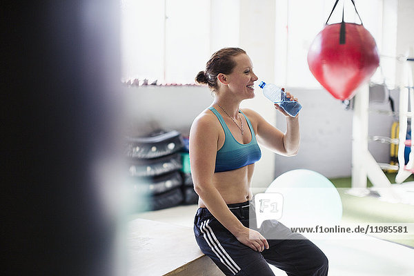 Female boxer drinking water and resting post workout in gym