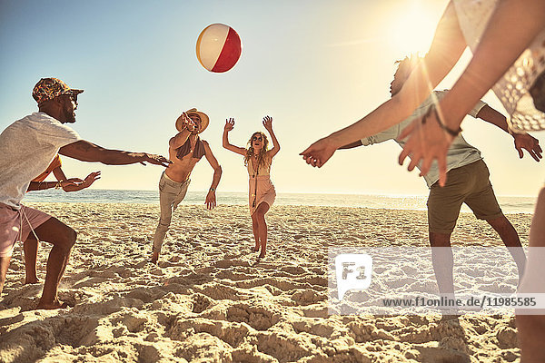 Verspielte junge Freunde spielen mit Beachball am sonnigen Sommerstrand