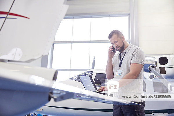 Flugzeugmechaniker beim Telefonieren und Arbeiten am Laptop im Hangar